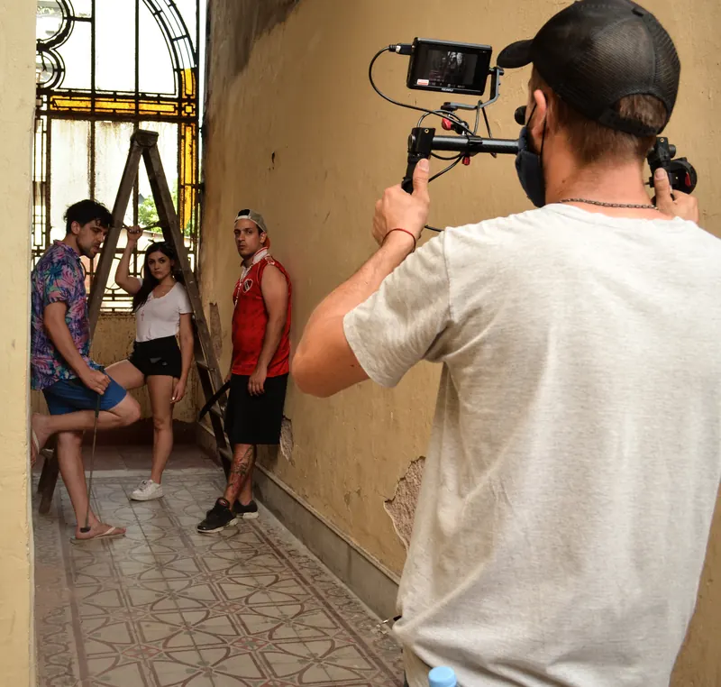Un camarógrafo con estabilizador filma a tres integrantes del elenco en un pasillo con piso de mosaicos.