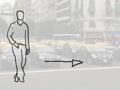 Un hombre camina hacia la derecha por una avenida llena de taxis.
