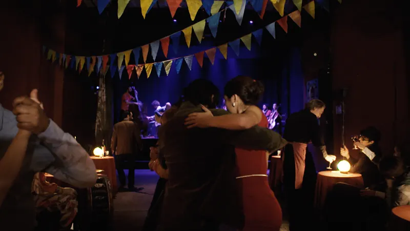 Parejas bailando tango entre las mesas iluminadas de la milonga.